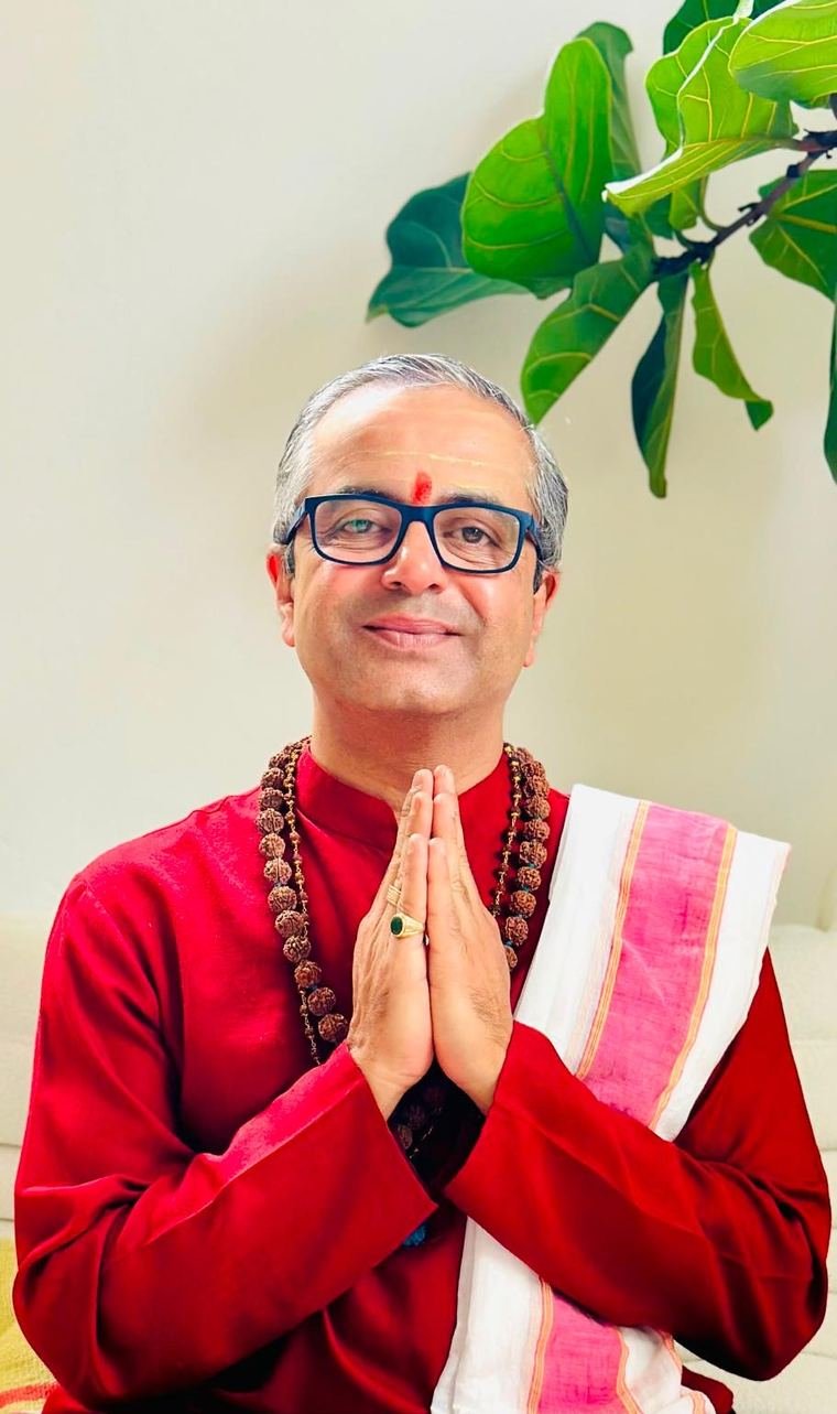 Pandit Brijesh Raval in a red kurta, hands joined in namaste