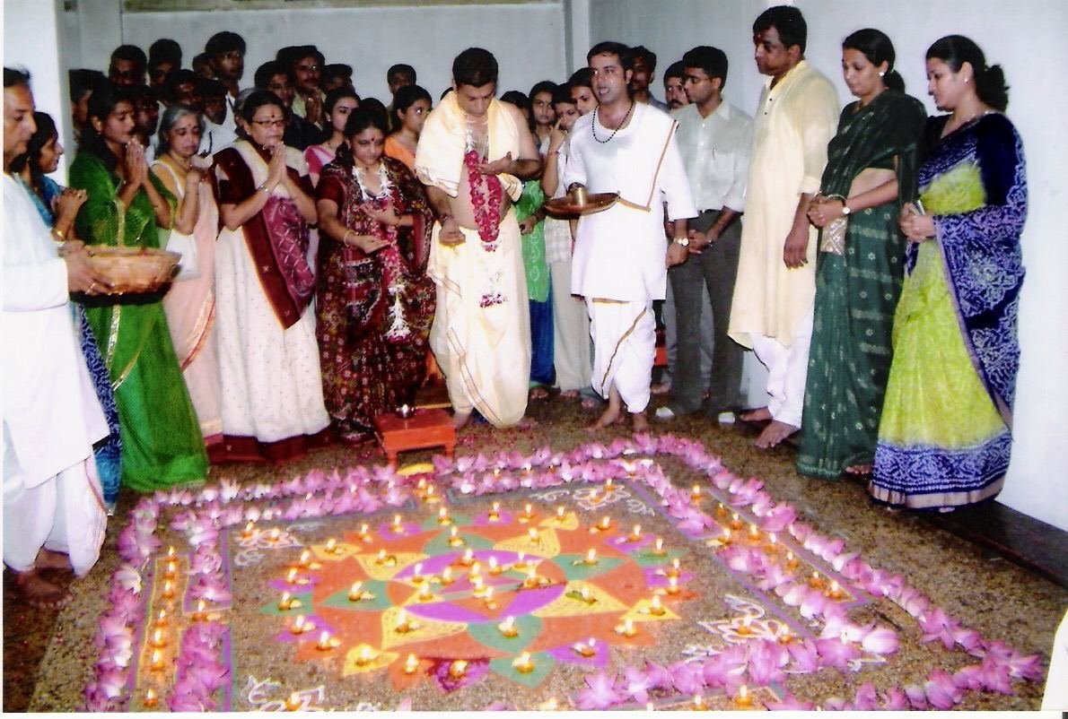 Devotees around a rangoli bordered with lotus flowers and diyas